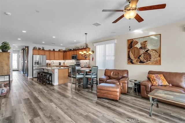 living room featuring sink, ceiling fan with notable chandelier, and light hardwood / wood-style flooring