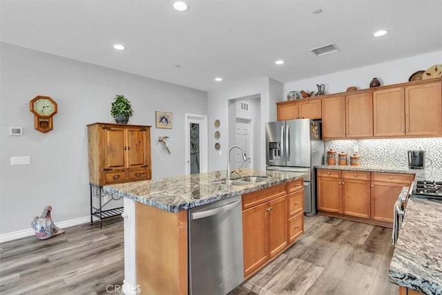 kitchen with appliances with stainless steel finishes, sink, light stone counters, and an island with sink