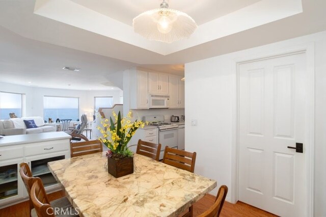 dining space with a raised ceiling and light wood-type flooring