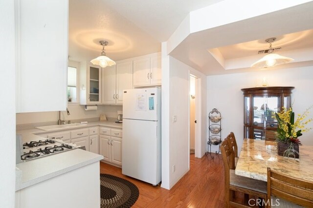 kitchen with white appliances, sink, hanging light fixtures, light hardwood / wood-style flooring, and white cabinetry