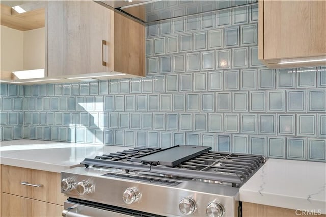 details with light stone counters, light brown cabinetry, gas stove, and decorative backsplash