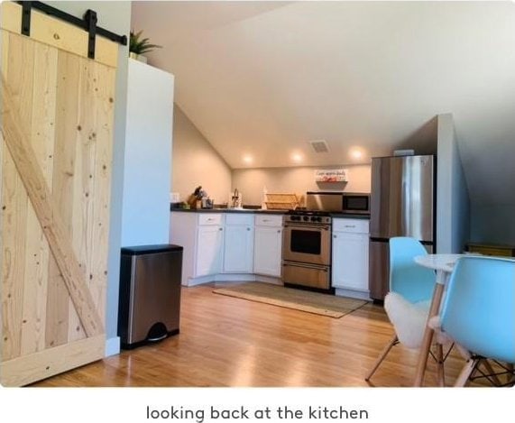 kitchen featuring stainless steel appliances, a barn door, light hardwood / wood-style floors, lofted ceiling, and white cabinets