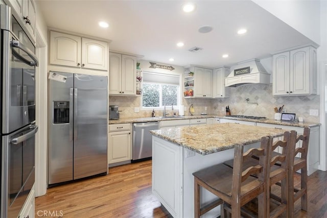 kitchen with a kitchen bar, custom range hood, stainless steel appliances, sink, and a center island