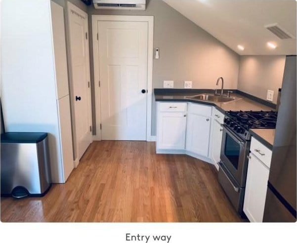 kitchen with an AC wall unit, sink, light hardwood / wood-style flooring, white cabinetry, and stainless steel appliances