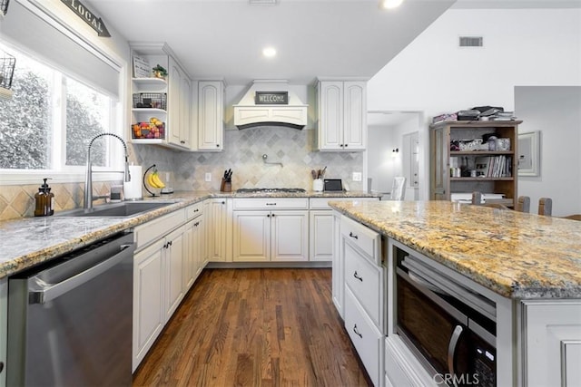 kitchen with light stone countertops, custom exhaust hood, stainless steel appliances, sink, and white cabinetry