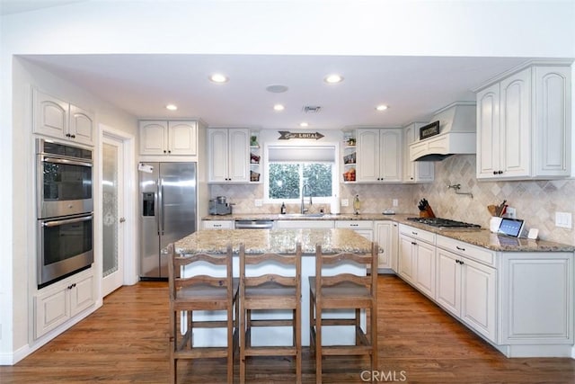 kitchen featuring white cabinetry, stainless steel appliances, a breakfast bar area, a kitchen island, and custom exhaust hood