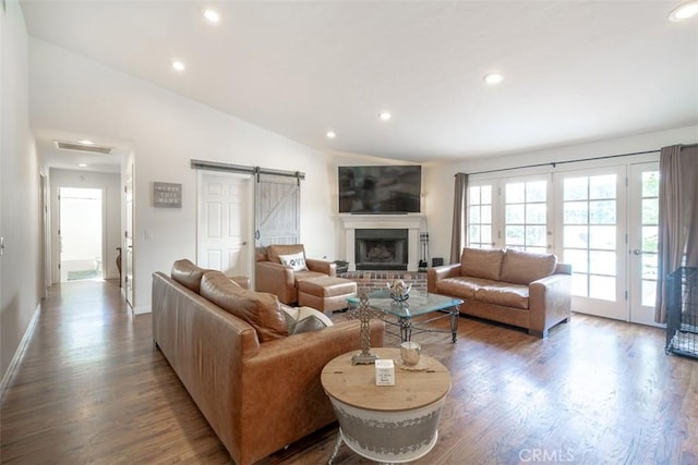 living room with hardwood / wood-style flooring, a barn door, lofted ceiling, and a brick fireplace