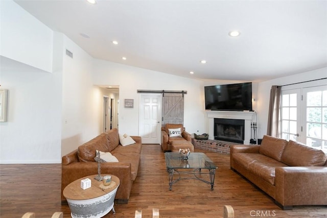 living room with a barn door, a fireplace, wood-type flooring, and vaulted ceiling