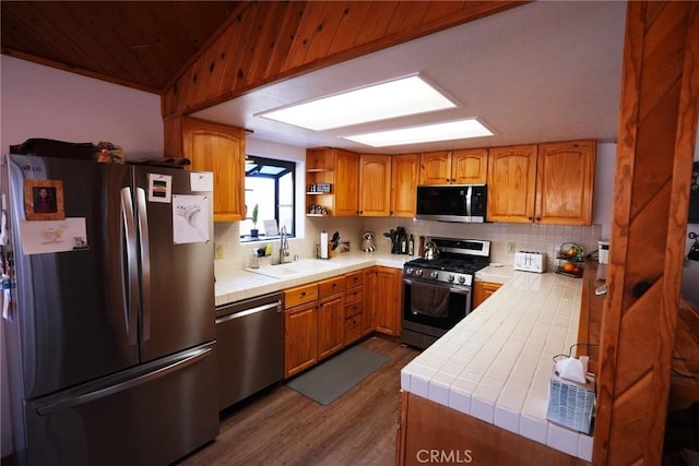 kitchen with backsplash, wood-type flooring, sink, stainless steel appliances, and tile counters