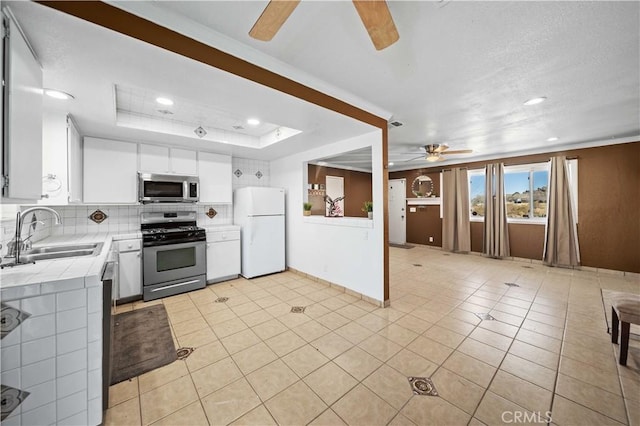 kitchen with appliances with stainless steel finishes, sink, white cabinetry, tile counters, and light tile patterned flooring