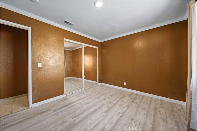 unfurnished bedroom with light wood-type flooring, ornamental molding, and a closet