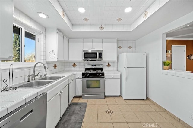 kitchen with tile countertops, a raised ceiling, sink, appliances with stainless steel finishes, and white cabinetry