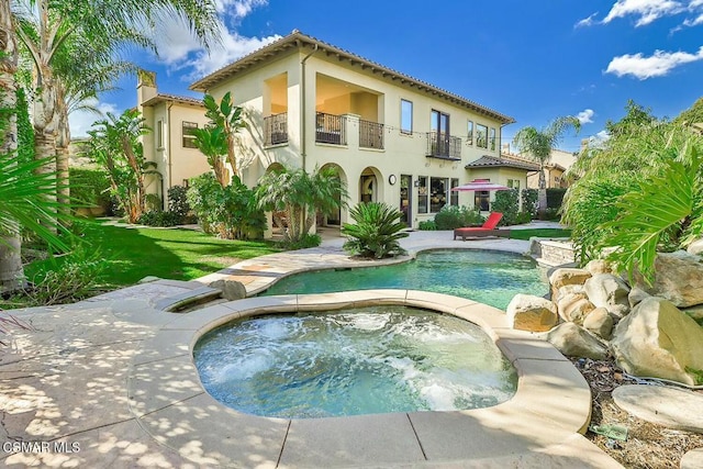 rear view of house with a balcony and a pool with hot tub