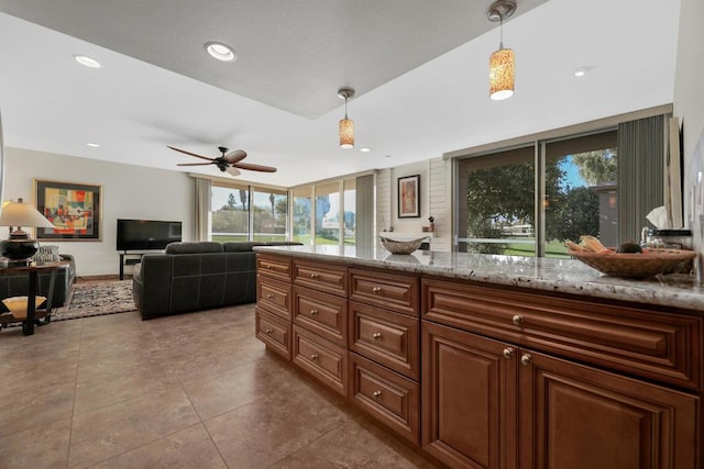 kitchen with hanging light fixtures, tile patterned floors, light stone countertops, and ceiling fan