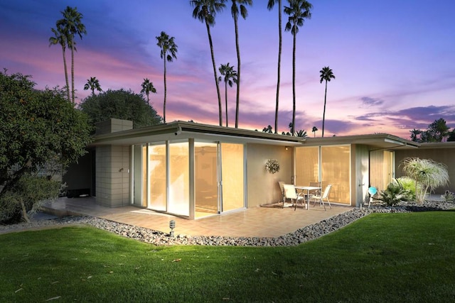 back house at dusk with a patio and a yard