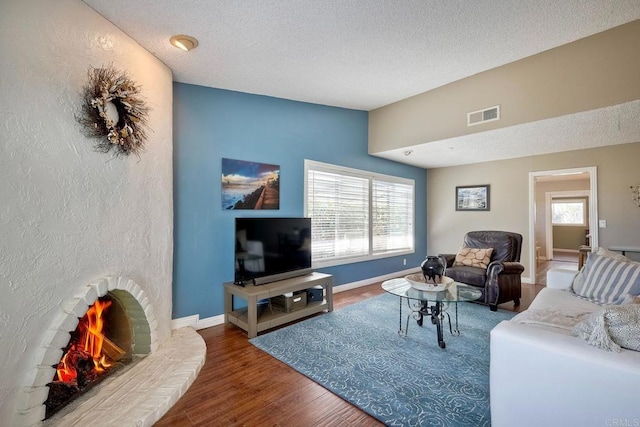 living area featuring wood finished floors, baseboards, visible vents, a lit fireplace, and a textured ceiling