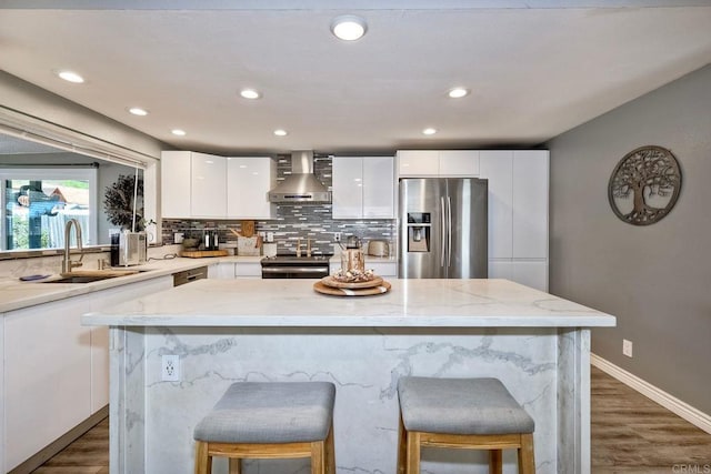 kitchen with modern cabinets, a sink, stainless steel appliances, wall chimney range hood, and decorative backsplash