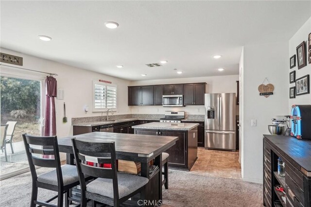 kitchen featuring stainless steel appliances, a sink, visible vents, dark brown cabinets, and a center island