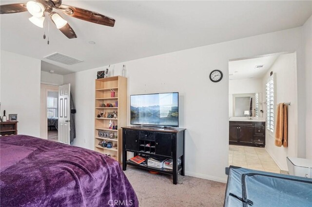 bedroom with ceiling fan, light colored carpet, visible vents, baseboards, and ensuite bath