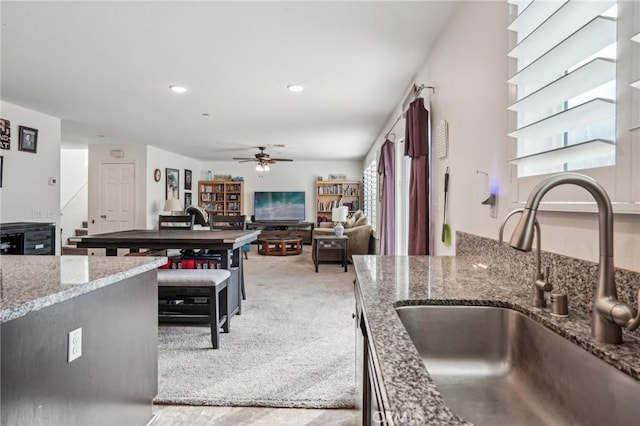 kitchen with ceiling fan, stone counters, recessed lighting, light carpet, and a sink