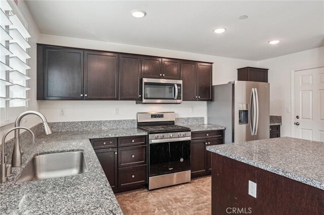 kitchen featuring recessed lighting, appliances with stainless steel finishes, a sink, dark brown cabinetry, and light stone countertops