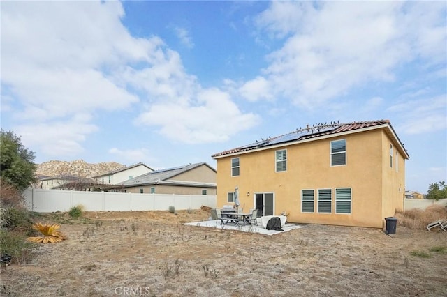 rear view of house featuring a fenced backyard, a patio area, roof mounted solar panels, and stucco siding