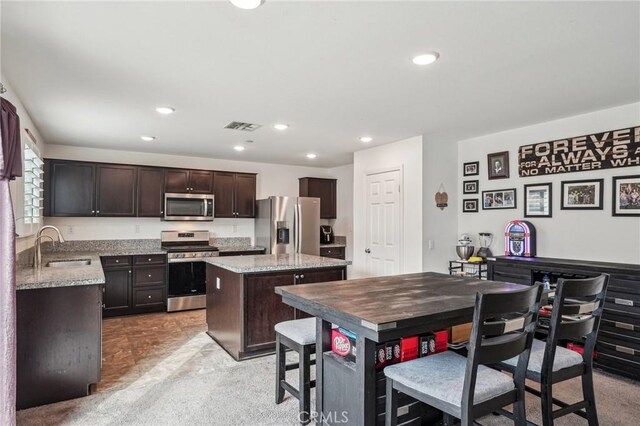 kitchen featuring a center island, visible vents, appliances with stainless steel finishes, a sink, and dark brown cabinetry