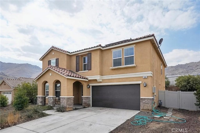 mediterranean / spanish house featuring stone siding, fence, concrete driveway, and stucco siding