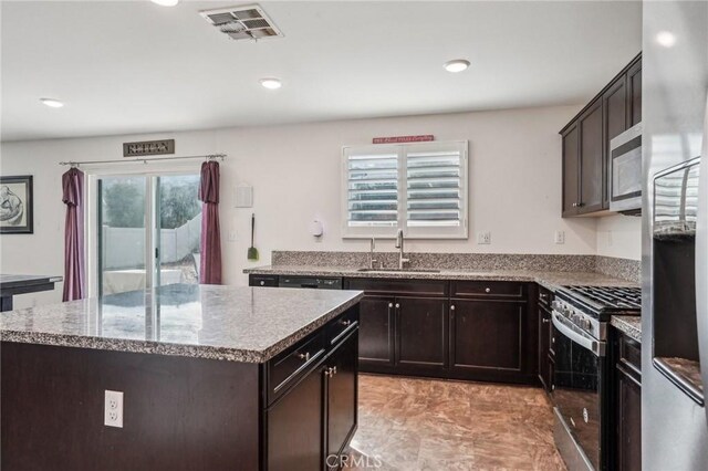 kitchen featuring stone countertops, visible vents, a kitchen island, stainless steel appliances, and a sink