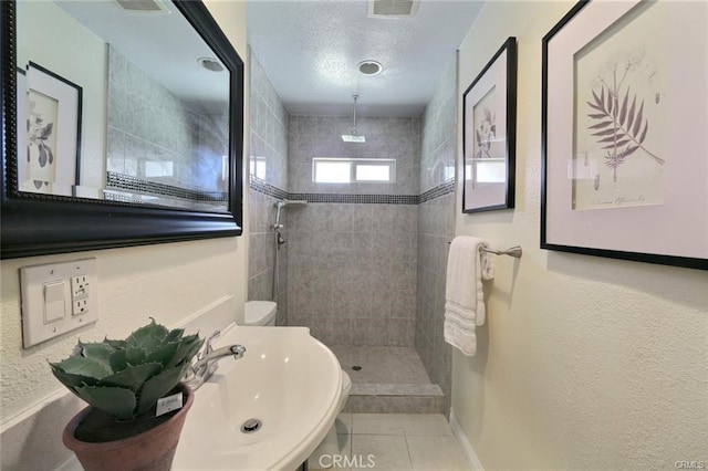 bathroom featuring a textured ceiling, tile patterned flooring, tiled shower, and sink