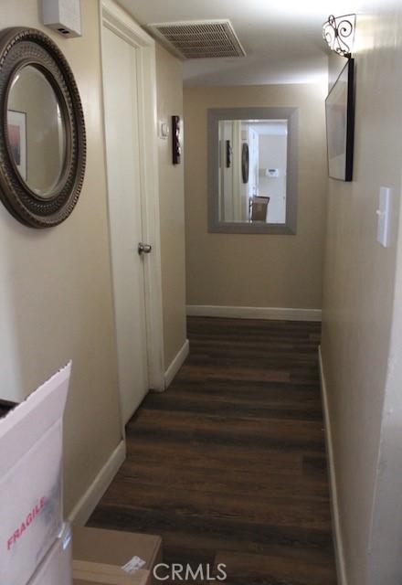 hallway featuring dark wood finished floors, visible vents, and baseboards