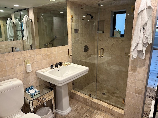 bathroom featuring sink, toilet, a shower with door, and tile walls