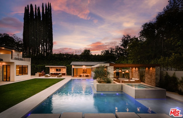 pool at dusk with an in ground hot tub, a patio, exterior fireplace, and a lawn