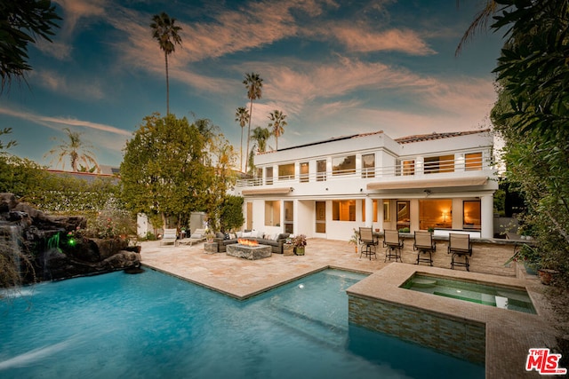 back house at dusk with a pool with hot tub, exterior bar, a fire pit, and a patio