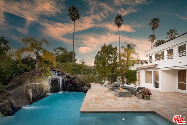 pool at dusk with pool water feature, an outdoor living space, and a patio area