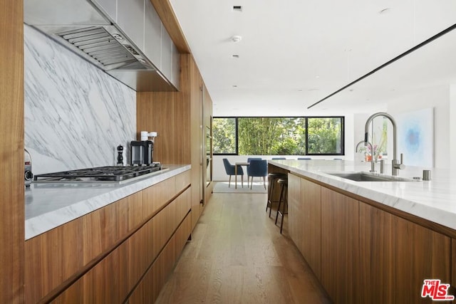 kitchen featuring light stone countertops, sink, stainless steel gas cooktop, light hardwood / wood-style floors, and exhaust hood