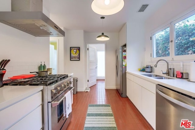 kitchen featuring appliances with stainless steel finishes, wall chimney exhaust hood, sink, decorative light fixtures, and white cabinetry