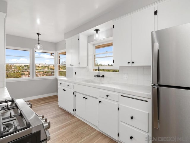 kitchen with pendant lighting, sink, appliances with stainless steel finishes, white cabinets, and tile countertops