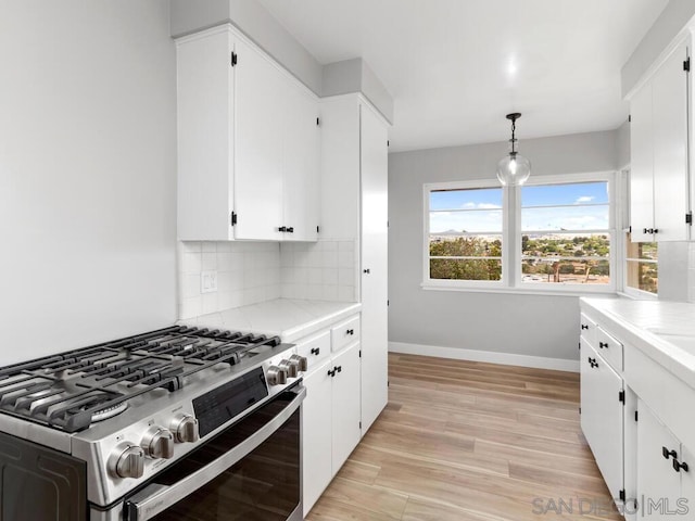 kitchen with decorative light fixtures, tasteful backsplash, white cabinets, gas stove, and light wood-type flooring