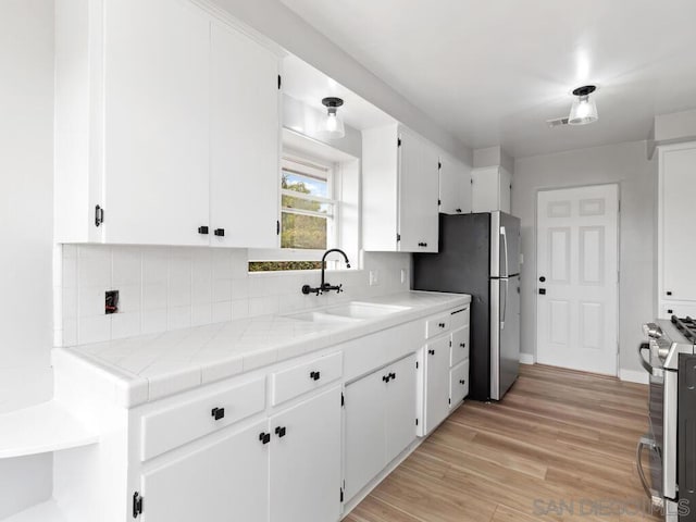 kitchen with appliances with stainless steel finishes, tile countertops, white cabinetry, sink, and light hardwood / wood-style floors