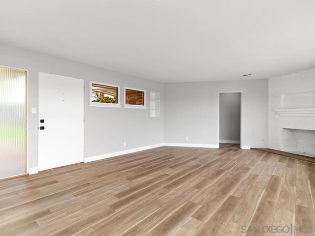 unfurnished living room featuring a brick fireplace and light hardwood / wood-style flooring