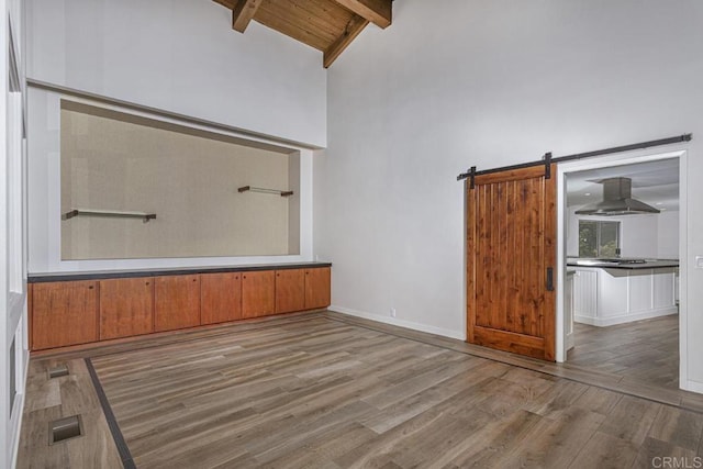 interior space featuring beamed ceiling, a barn door, light wood-type flooring, and high vaulted ceiling