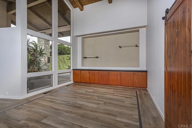 unfurnished room with beam ceiling, wooden ceiling, a barn door, light hardwood / wood-style flooring, and high vaulted ceiling