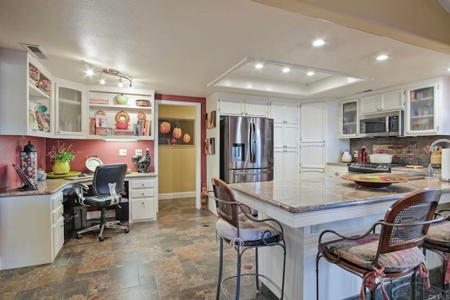 kitchen featuring decorative backsplash, appliances with stainless steel finishes, light stone counters, a tray ceiling, and white cabinets