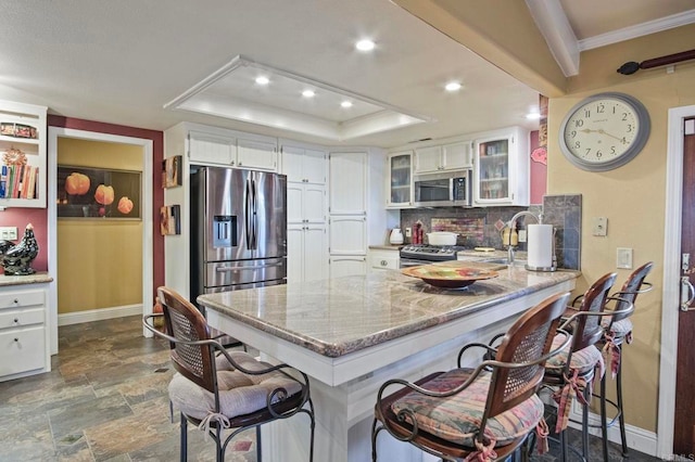 kitchen featuring stainless steel appliances, kitchen peninsula, a tray ceiling, white cabinets, and a kitchen bar