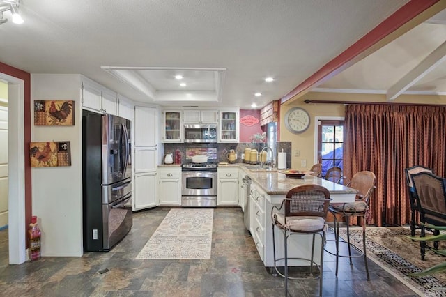 kitchen featuring white cabinets, sink, decorative backsplash, appliances with stainless steel finishes, and a breakfast bar area