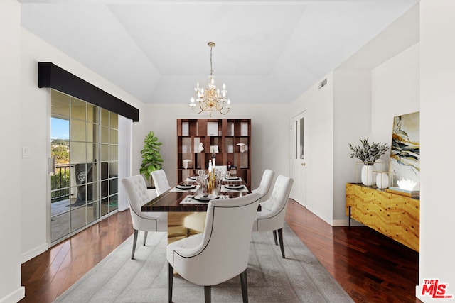 dining room with a raised ceiling, dark wood-type flooring, and an inviting chandelier