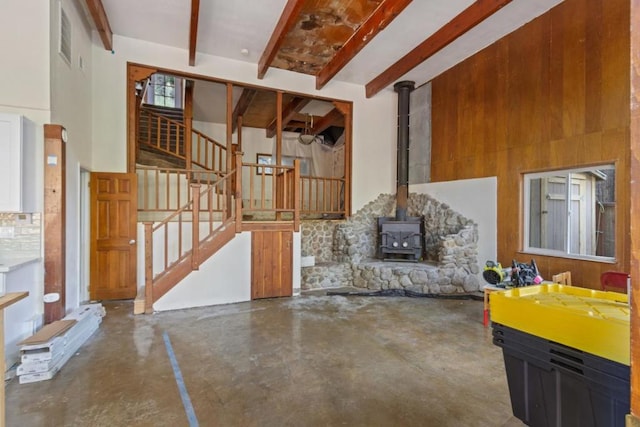 living room featuring a towering ceiling, a wood stove, beamed ceiling, and concrete flooring