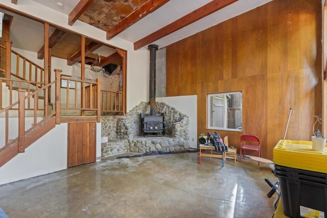 interior space featuring a towering ceiling, concrete floors, wooden walls, a wood stove, and beam ceiling