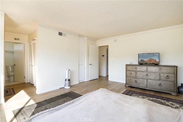 bedroom featuring ensuite bathroom, a textured ceiling, ornamental molding, and light hardwood / wood-style flooring